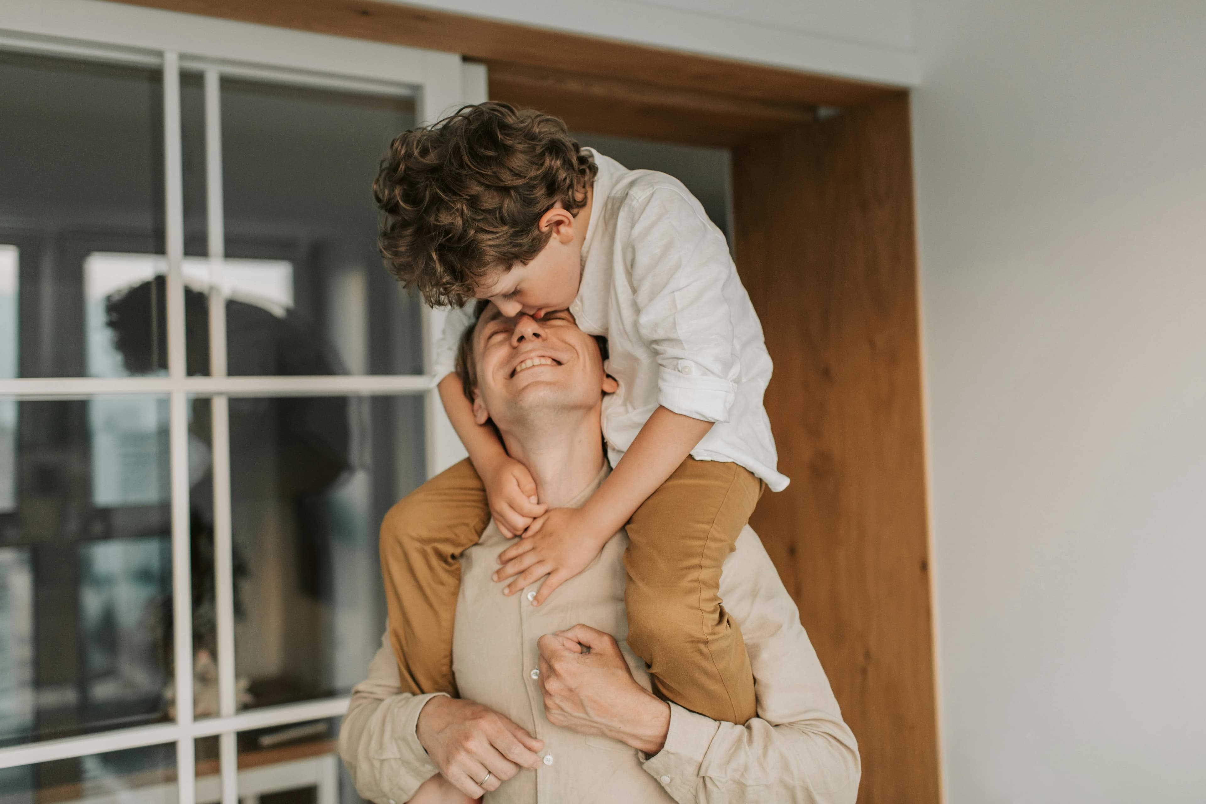 A father laughing with his son on his shoulders at home